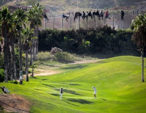 José Palazon/Reuters African asylum seekers stuck on a razor wire fence, behind white-clad golfers teeing off on a golf course.